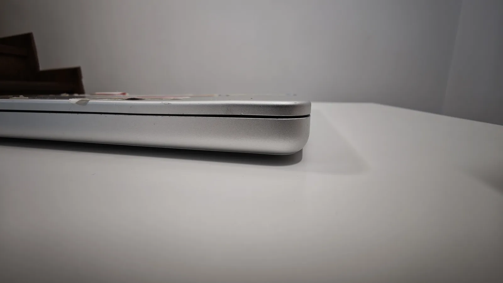 MacBook Pro 14 închis, văzut din lateral: colțul capacului deformat după lovitură, cu spațiu între capac și carcasă